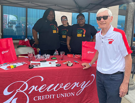 Three women manning a Brewery Credit Union booth and older man visiting from front