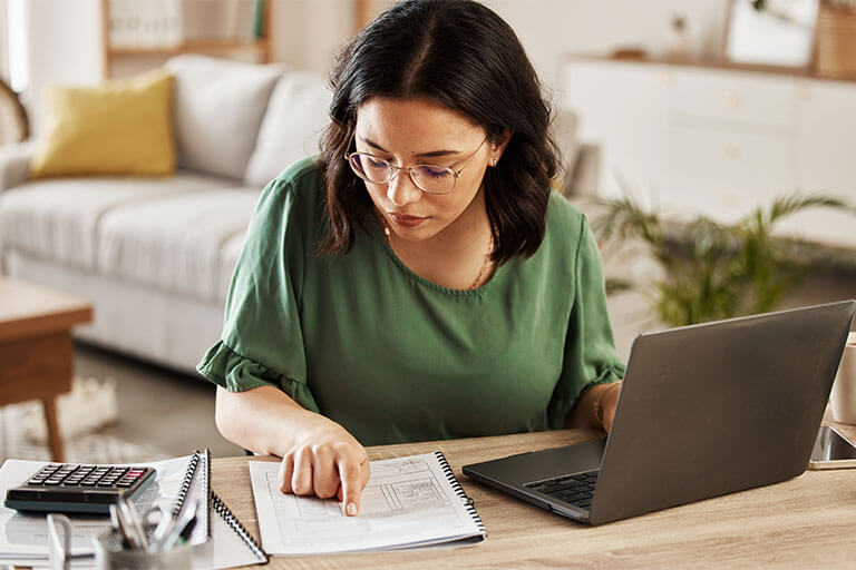 Woman reviewing document while sitting at desk with laptop and calculator
