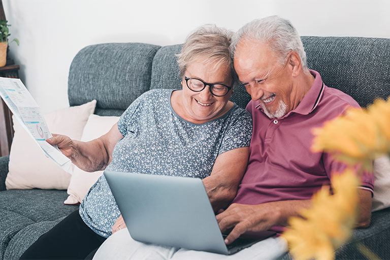 Older couple sitting next to each other on couch looking at computer screen